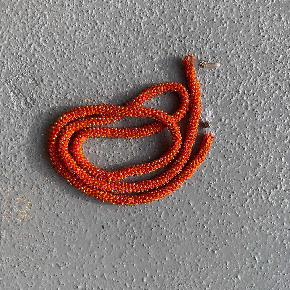 A coiled orange beaded necklace or cord laid on a textured gray concrete surface.