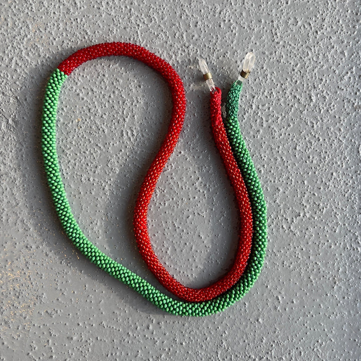 A braided rope or cord laid on a textured gray surface, forming an S-shape. The rope is primarily red and green, with small white tips at the ends.