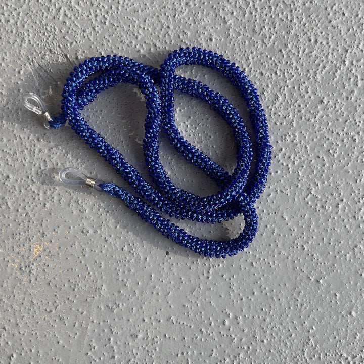 A coiled blue braided rope or leash with clear plastic loops at both ends, resting on a textured gray concrete surface.