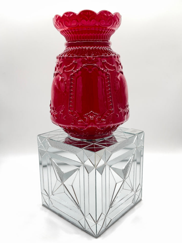 A glossy red embossed glass vase with a scalloped flared rim, displayed on a clear faceted glass pedestal against a light gray studio background.