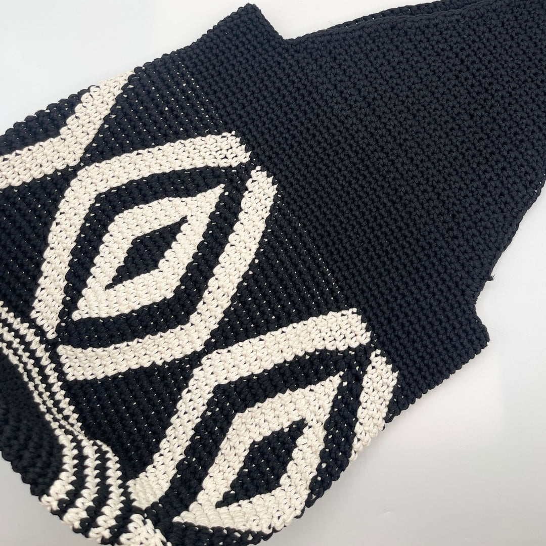 A close-up of a black knit textile featuring a cream-colored geometric diamond pattern, laid flat on a white background.