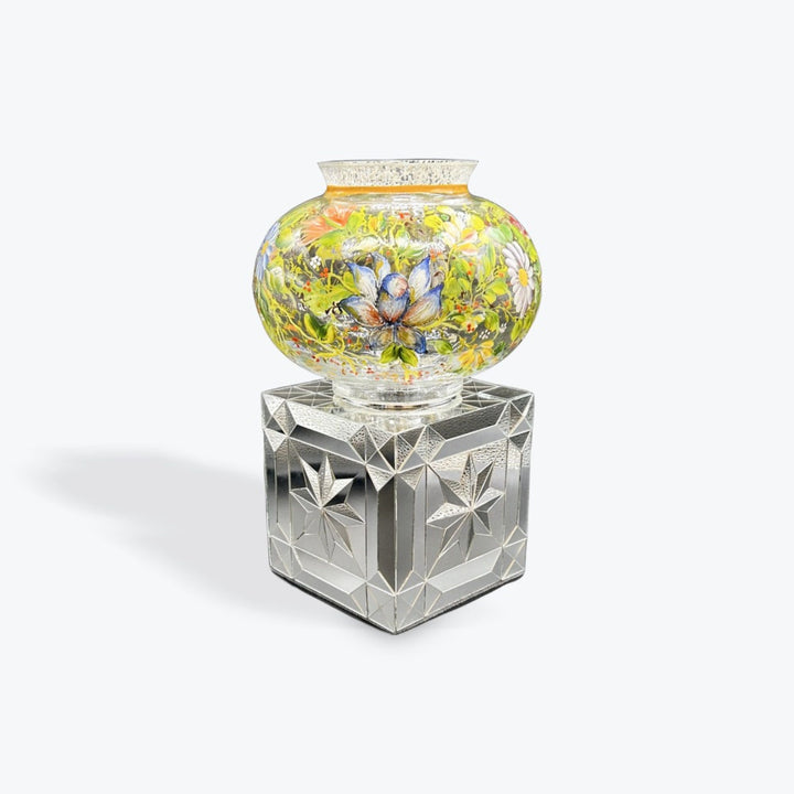 A decorative glass vase with a colorful floral pattern, displayed on a faceted clear glass pedestal against a light gray background.