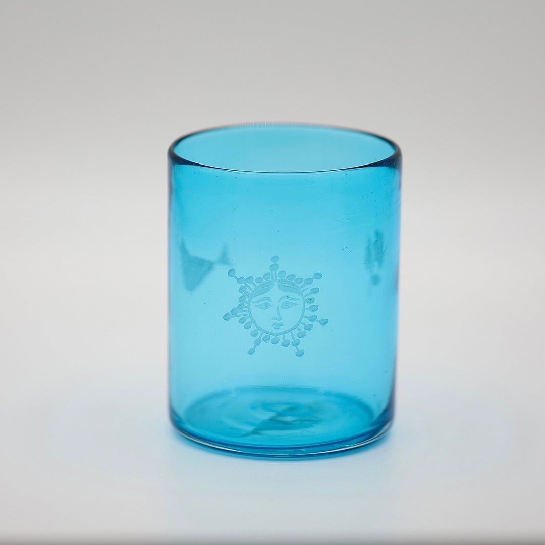 Blue glass tumbler with a sun design on a light gray background