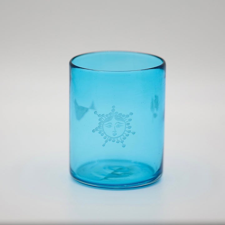 Blue glass tumbler with a sun design on a light gray background