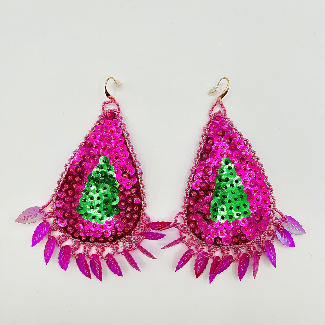 A pair of teardrop-shaped dangling earrings with bright pink sequins, a green sequin Christmas tree motif in the center, and dangling magenta leaf-like spikes along the bottom, shown on a plain light background.