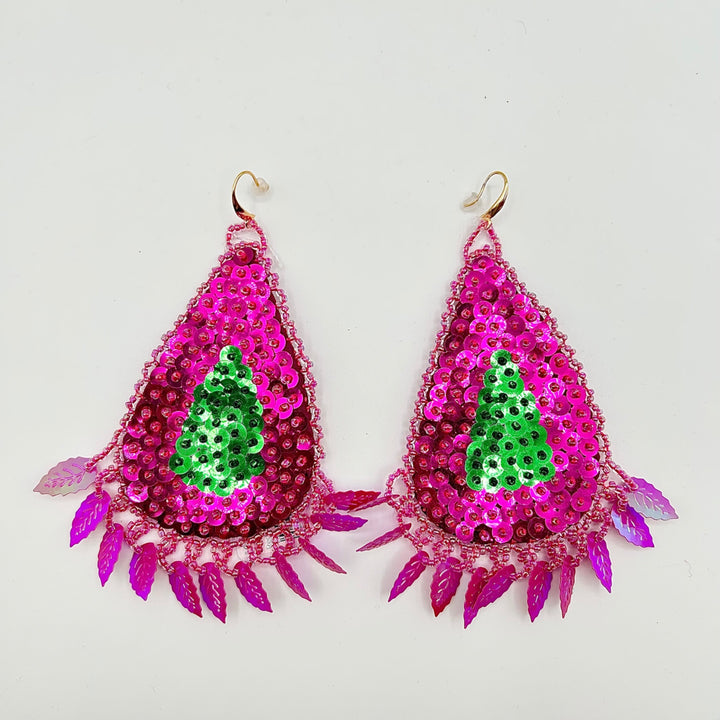 A pair of teardrop-shaped dangling earrings with bright pink sequins, a green sequin Christmas tree motif in the center, and dangling magenta leaf-like spikes along the bottom, shown on a plain light background.