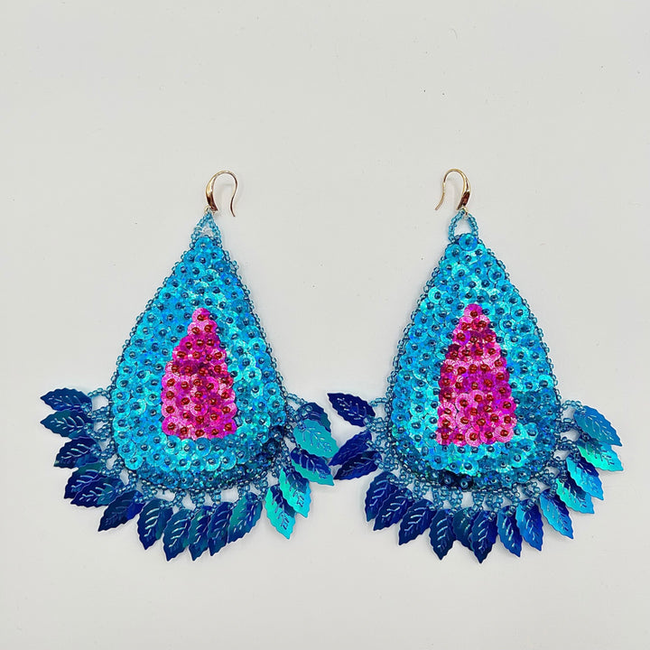 A pair of large, teardrop-shaped dangling earrings covered in sequins. The earrings feature a bright turquoise blue outer section with layered blue leaf-shaped sequins along the bottom, a central bright pink sequin teardrop, and gold-tone hook ear wires at the top, shown against a plain light gray background.