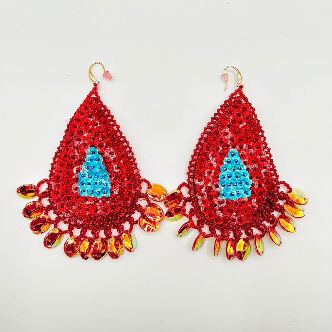 A pair of handmade beaded teardrop earrings featuring a bright red sequined body, a light blue sequined Christmas tree motif in the center, and dangling iridescent orange and yellow beads on gold-tone hooks, shown against a plain white background.