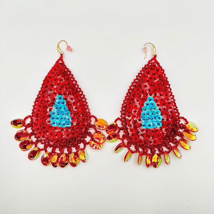 A pair of handmade beaded teardrop earrings featuring a bright red sequined body, a light blue sequined Christmas tree motif in the center, and dangling iridescent orange and yellow beads on gold-tone hooks, shown against a plain white background.