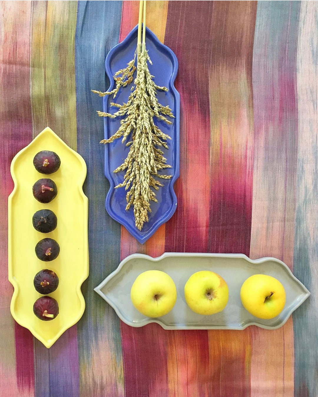 Three decorative trays with figs, wheat, and apples on a striped fabric background