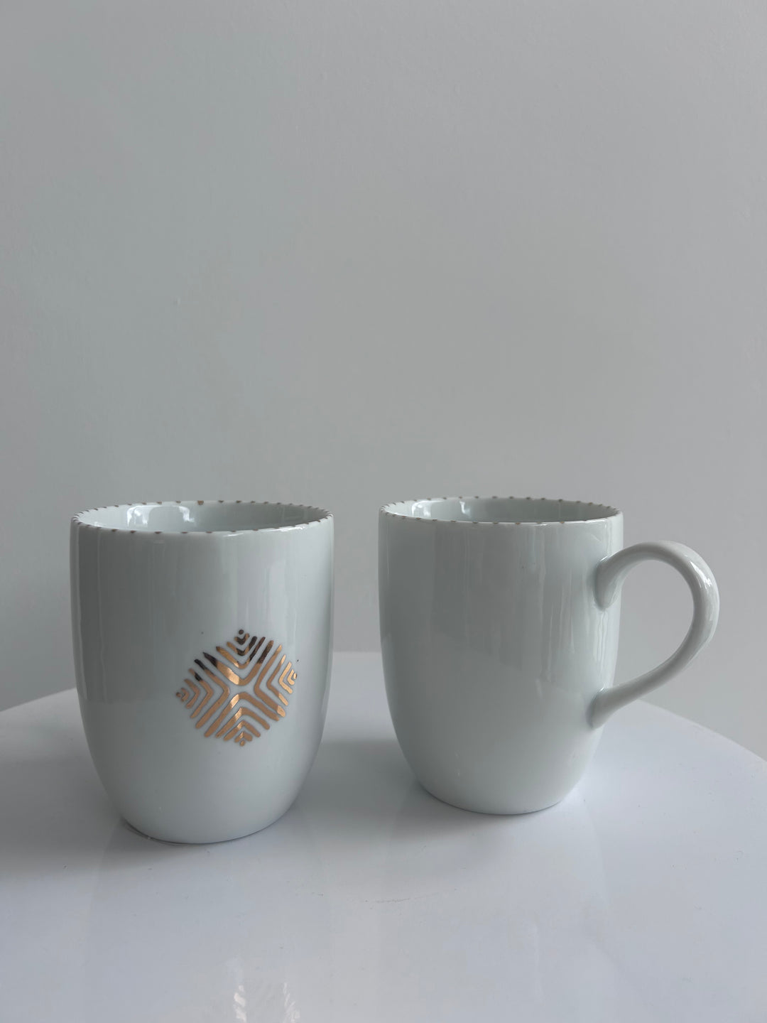 Two white wall-mounted cup holders with decorative cutouts on a light gray background