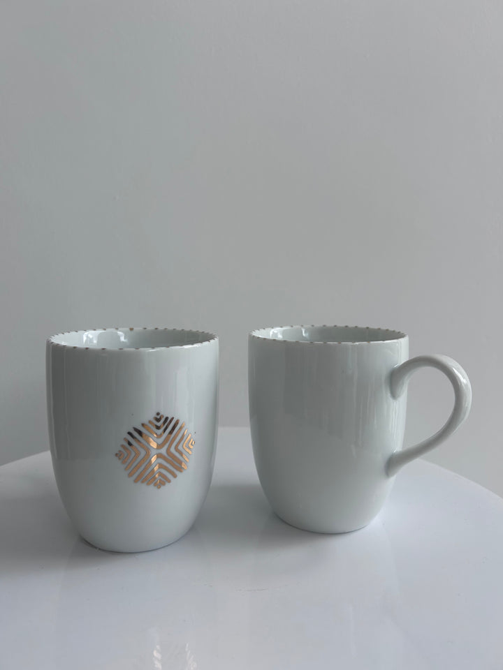 Two white wall-mounted cup holders with decorative cutouts on a light gray background