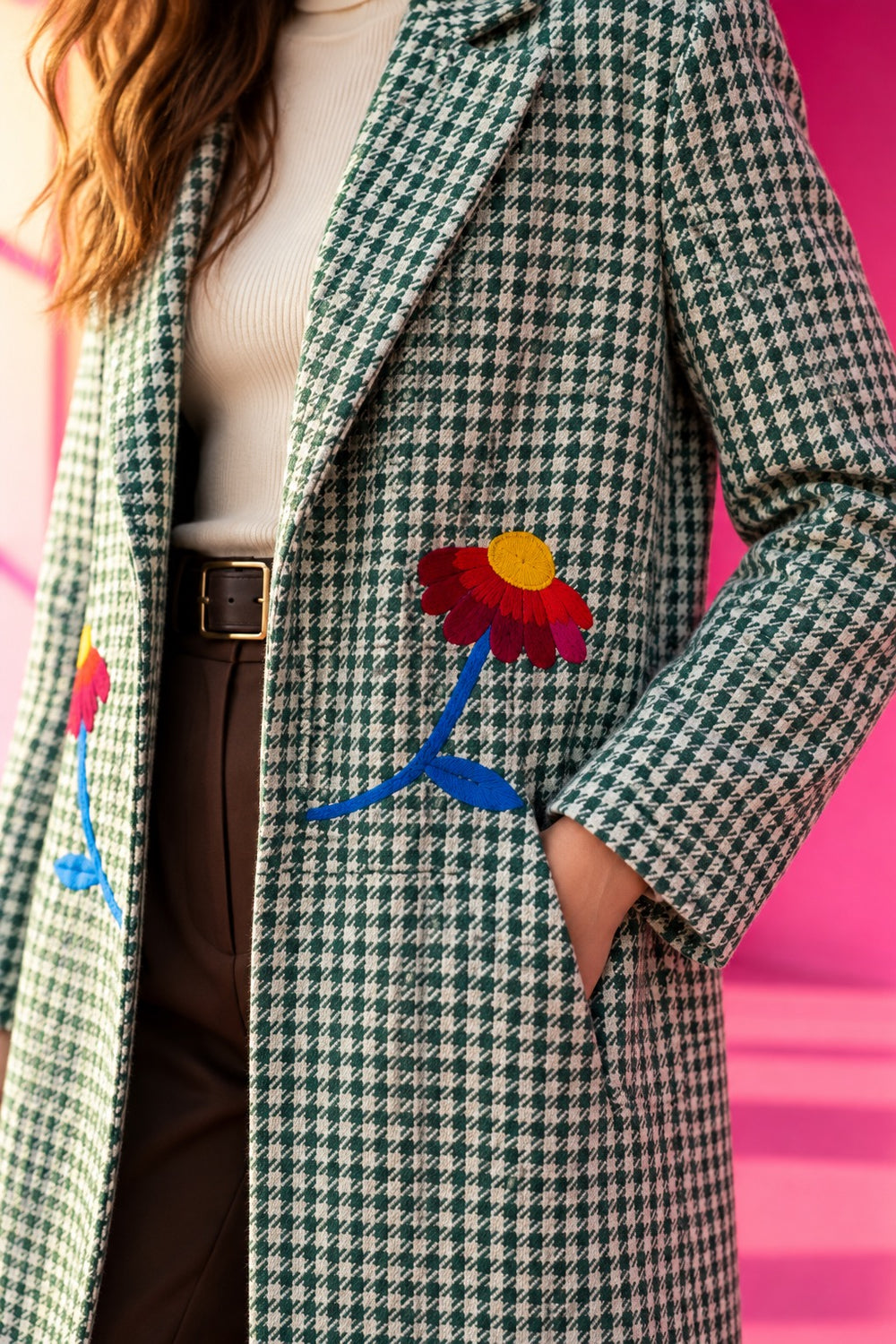 Close-up of a green and ivory plaid long coat featuring colorful hand-embroidered floral details and tailored lapels.